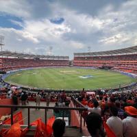 Crowd of orange-clad fans watches a cricket match from the stands at Rajiv Gandhi International Cricket Stadium.