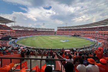 Crowd of orange-clad fans watches a cricket match from the stands at Rajiv Gandhi International Cricket Stadium.