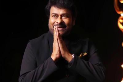 Chiranjeevi in a black bandhgala jacket, hands joined in a namaste greeting, against a dark stage background.