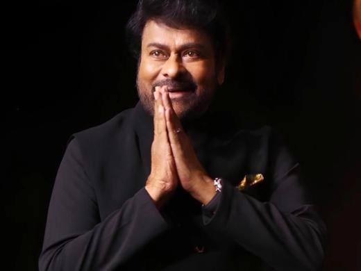 Chiranjeevi in a black bandhgala jacket, hands joined in a namaste greeting, against a dark stage background.