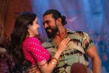 Janhvi Kapoor, in a pink blouse and gold jewellery, and Ram Charan, in a tie-dye shirt, smile at each other in a song from Peddi