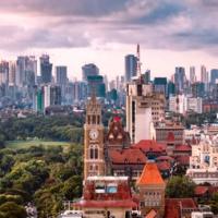 Mumbai cityscape with a clock tower, red-tiled roofs and a green field in front of distant high-rise towers