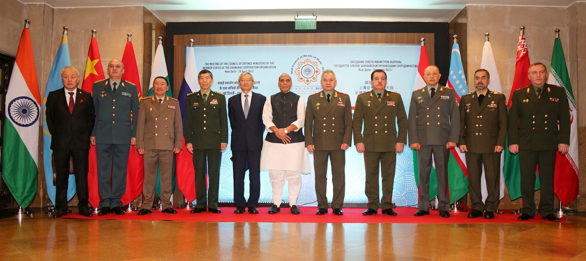 Defence ministers of SCO member states standing in a row before flags and a meeting backdrop, with Rajnath Singh in the centre
