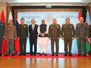 Defence ministers of SCO member states standing in a row before flags and a meeting backdrop, with Rajnath Singh in the centre