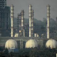Tall refinery columns and three white spherical storage tanks among processing structures and trees