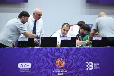 Officials and referees working at laptop scoring tables during a wrestling event, with purple event branding.