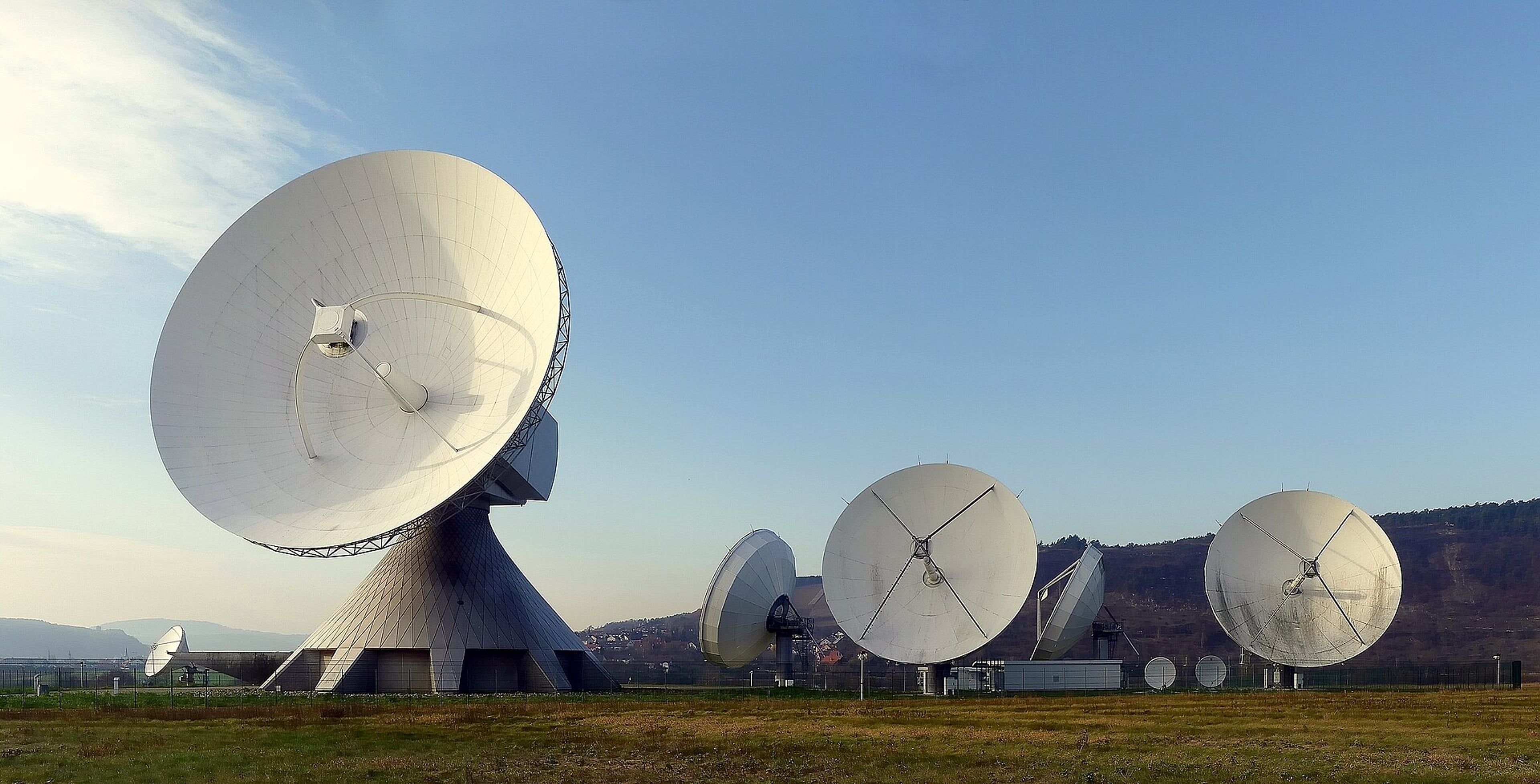 Large parabolic satellite dishes on a grassy field under a clear blue sky at an earth station