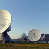 Large parabolic satellite dishes on a grassy field under a clear blue sky at an earth station