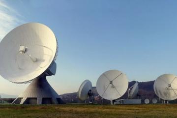 Large parabolic satellite dishes on a grassy field under a clear blue sky at an earth station