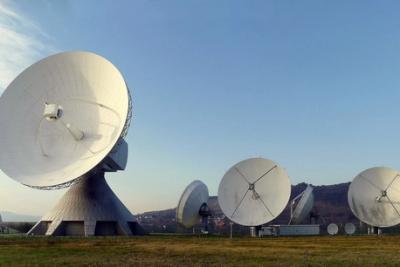 Large parabolic satellite dishes on a grassy field under a clear blue sky at an earth station