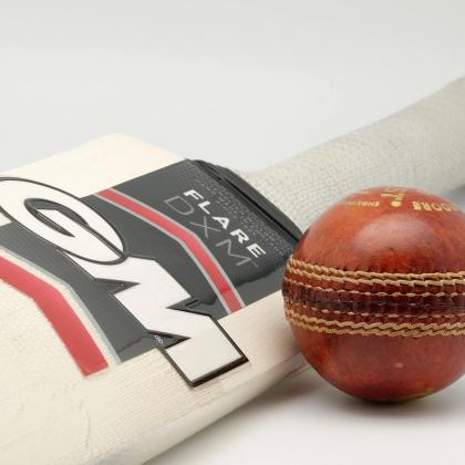 A cream cricket bat with a dark Flare DXM label and a red leather cricket ball on a plain light background.