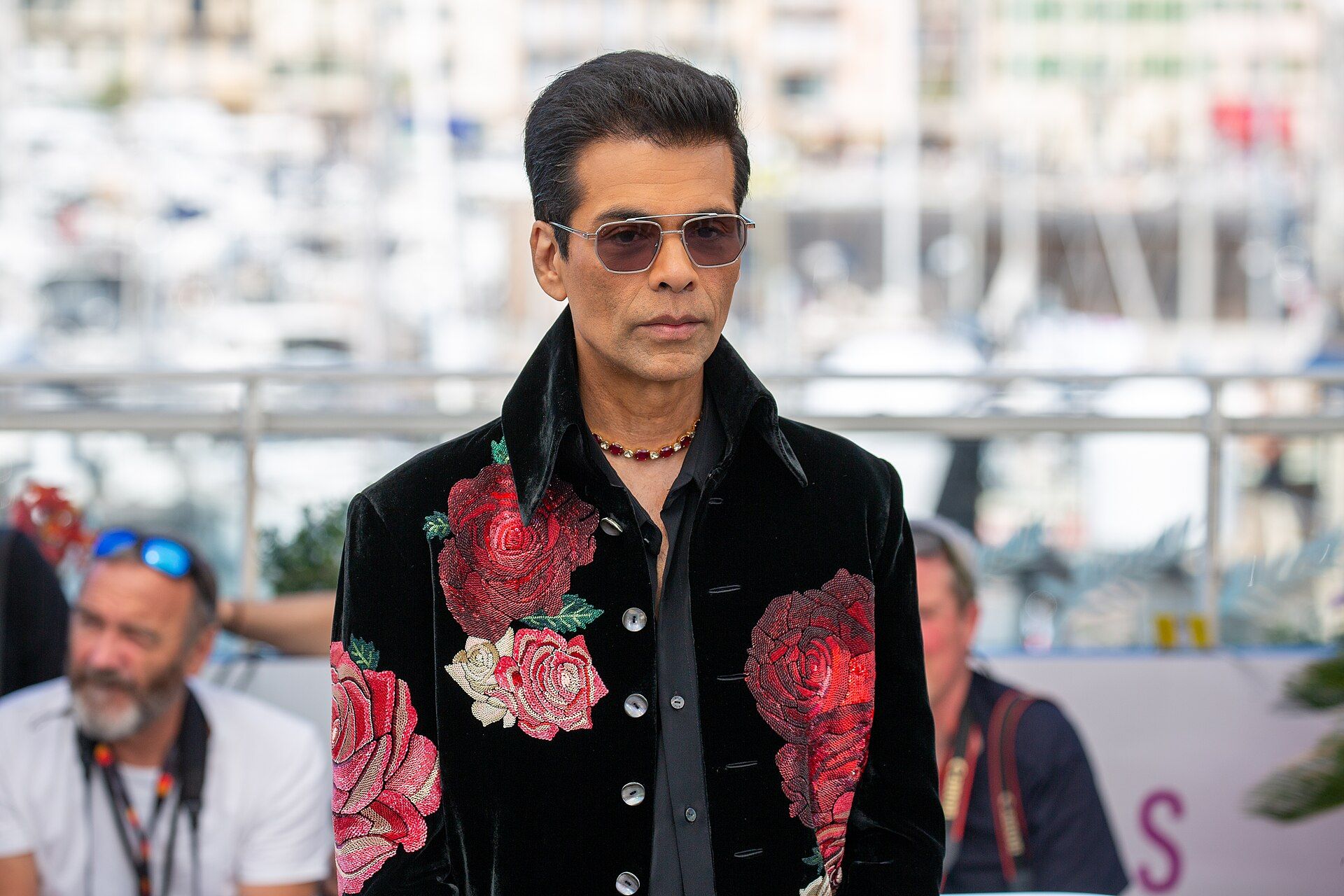 Man in sunglasses and a black velvet jacket embroidered with red roses, standing at an outdoor photocall