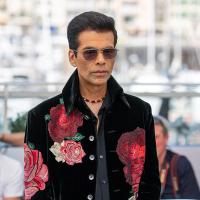 Man in sunglasses and a black velvet jacket embroidered with red roses, standing at an outdoor photocall