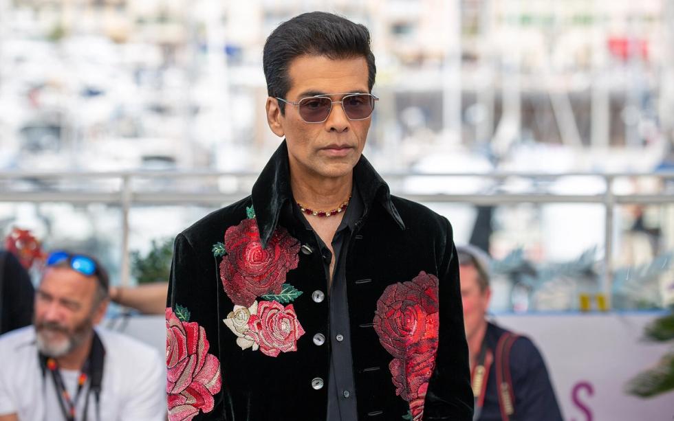 Man in sunglasses and a black velvet jacket embroidered with red roses, standing at an outdoor photocall