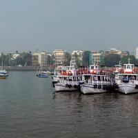 Panoramic view of Mumbai's waterfront with ferries and boats, the Taj Mahal Hotel and Gateway of India in haze.