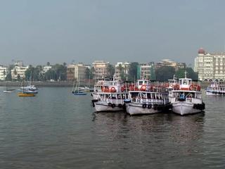 Panoramic view of Mumbai's waterfront with ferry boats on hazy water, the Taj hotel and Gateway of India.