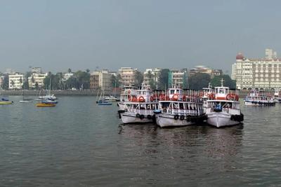 Panoramic view of Mumbai's waterfront with ferry boats on hazy water, the Taj hotel and Gateway of India.