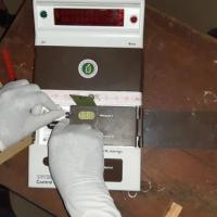 Gloved hands working on the control unit of an electronic voting machine on a wooden table.