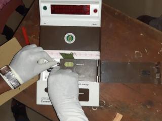 Gloved hands working on the control unit of an electronic voting machine on a wooden table.