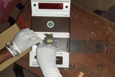 Gloved hands working on the control unit of an electronic voting machine on a wooden table.