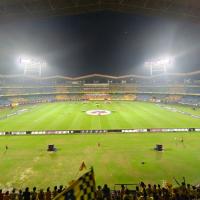 Floodlit football stadium at night with players on the pitch, Indian Super League boards and fans waving yellow flags