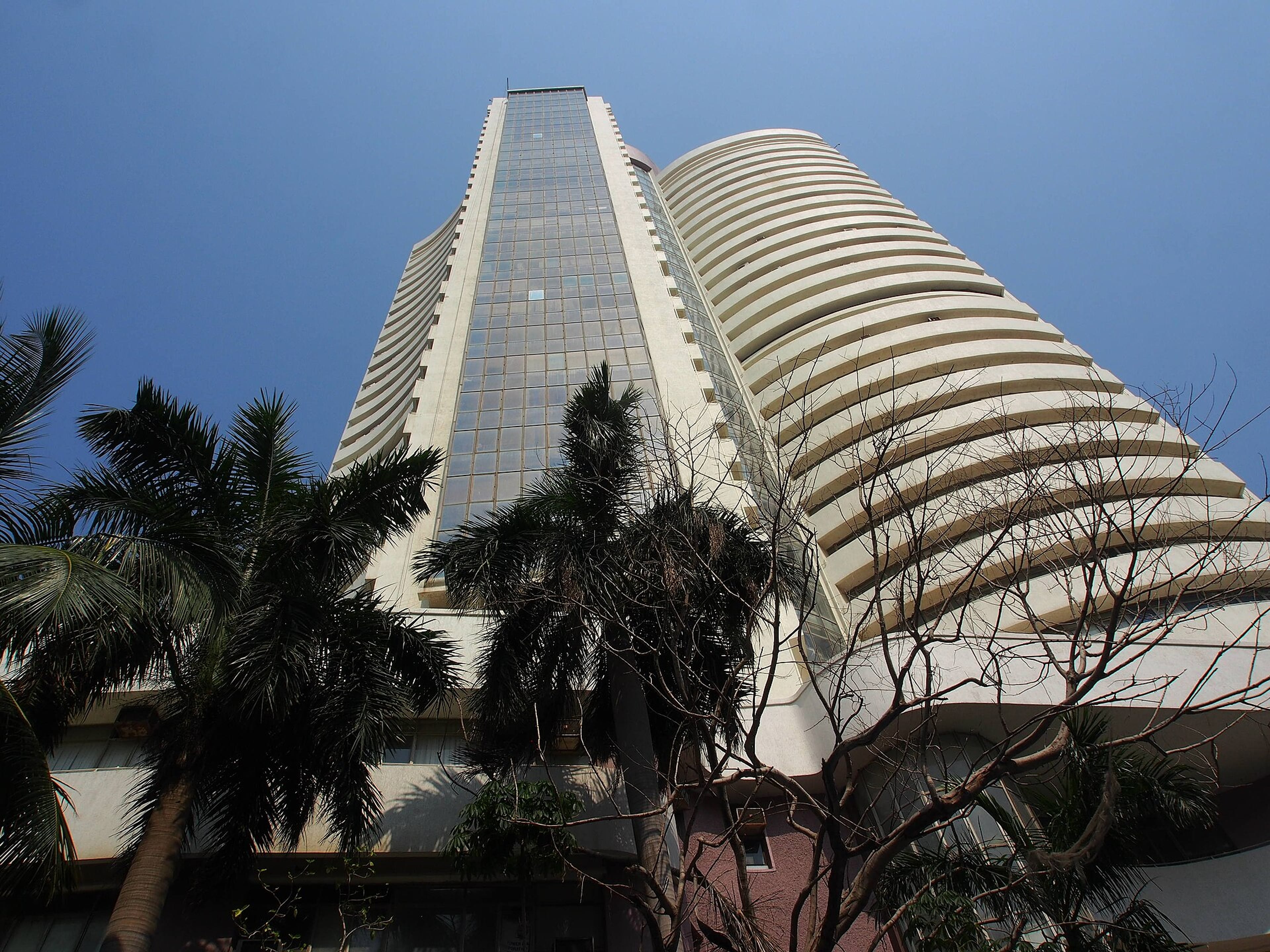 Low-angle view of a curved, tiered tower beside palm trees under a clear blue sky.