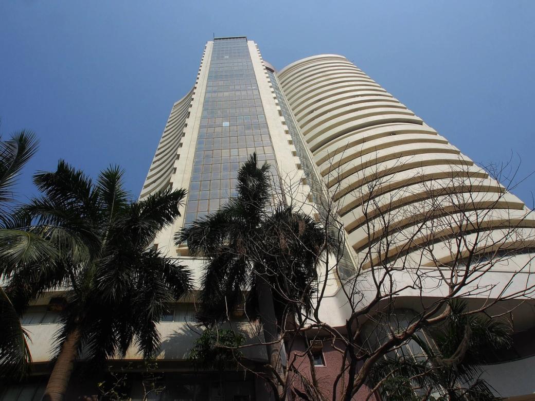Low-angle view of a curved, tiered tower beside palm trees under a clear blue sky.