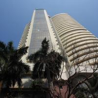 Low-angle view of a curved, tiered tower beside palm trees under a clear blue sky.