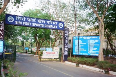 Entrance gate of the Siri Fort Sports Complex, with a blue sign, a welcome board and a facilities board under trees