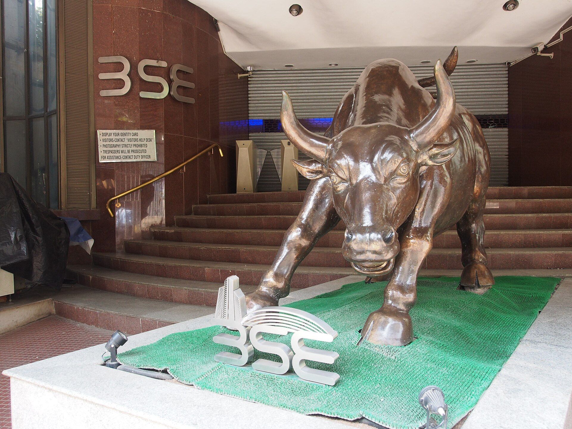Bronze bull statue on a green mat at the foot of a stone staircase, with BSE lettering on the wall behind