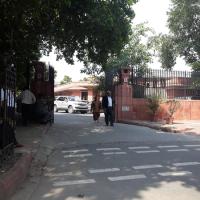 Entrance gate of the Supreme Court of India in New Delhi, with a parked car and people walking past under trees.