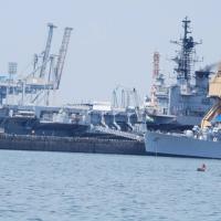 Indian Navy warships moored at a harbour quay beside port cranes, under a hazy sky.