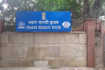Blue sign reading Prasar Bharati House in Hindi and English on a stone wall in front of trees