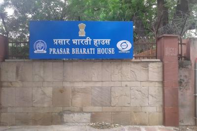 Blue sign reading Prasar Bharati House in Hindi and English on a stone wall in front of trees