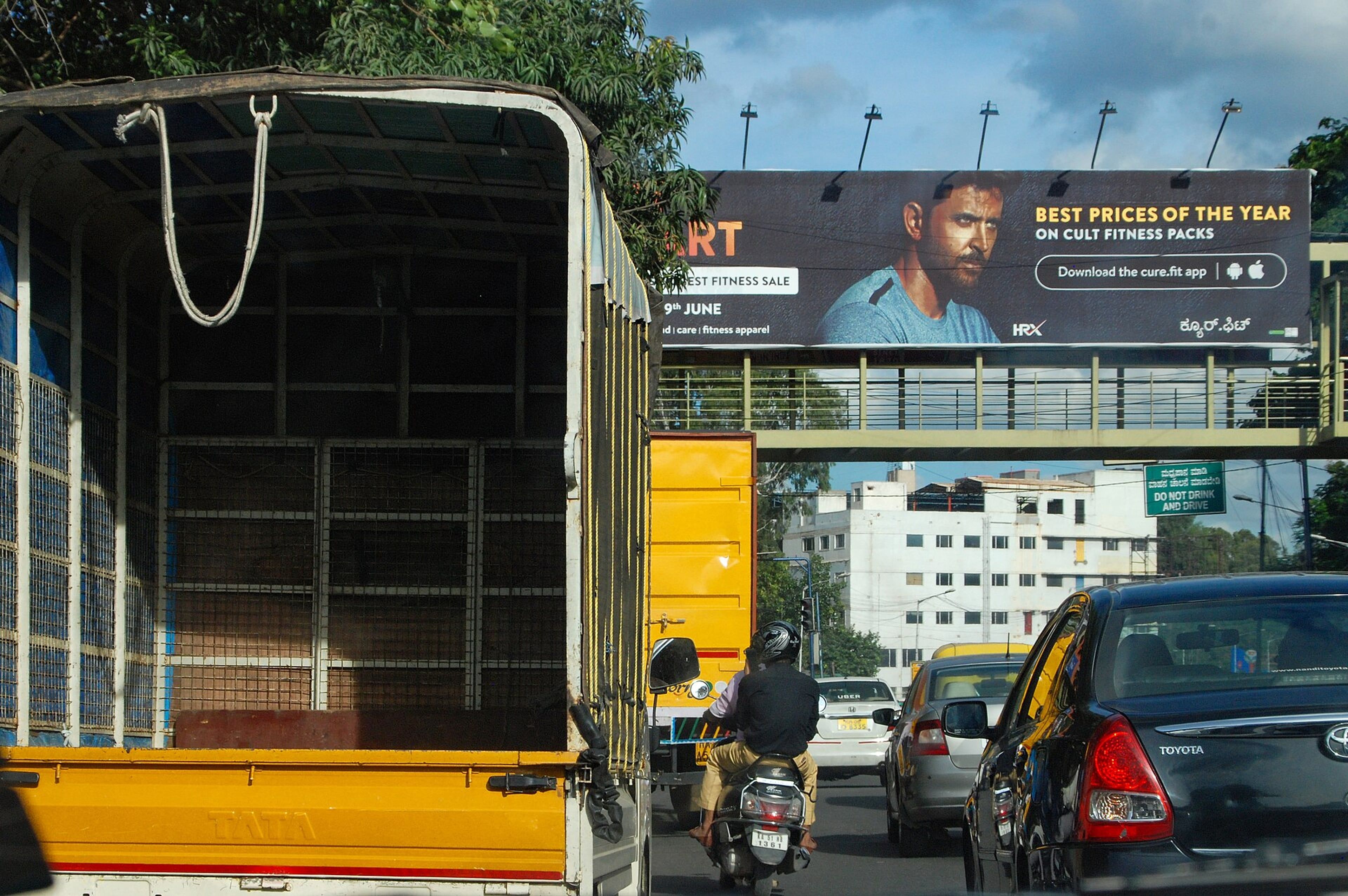 Billboard showing a man in a blue shirt above a busy road, with a truck, motorcycles and cars in traffic below