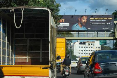Billboard showing a man in a blue shirt above a busy road, with a truck, motorcycles and cars in traffic below