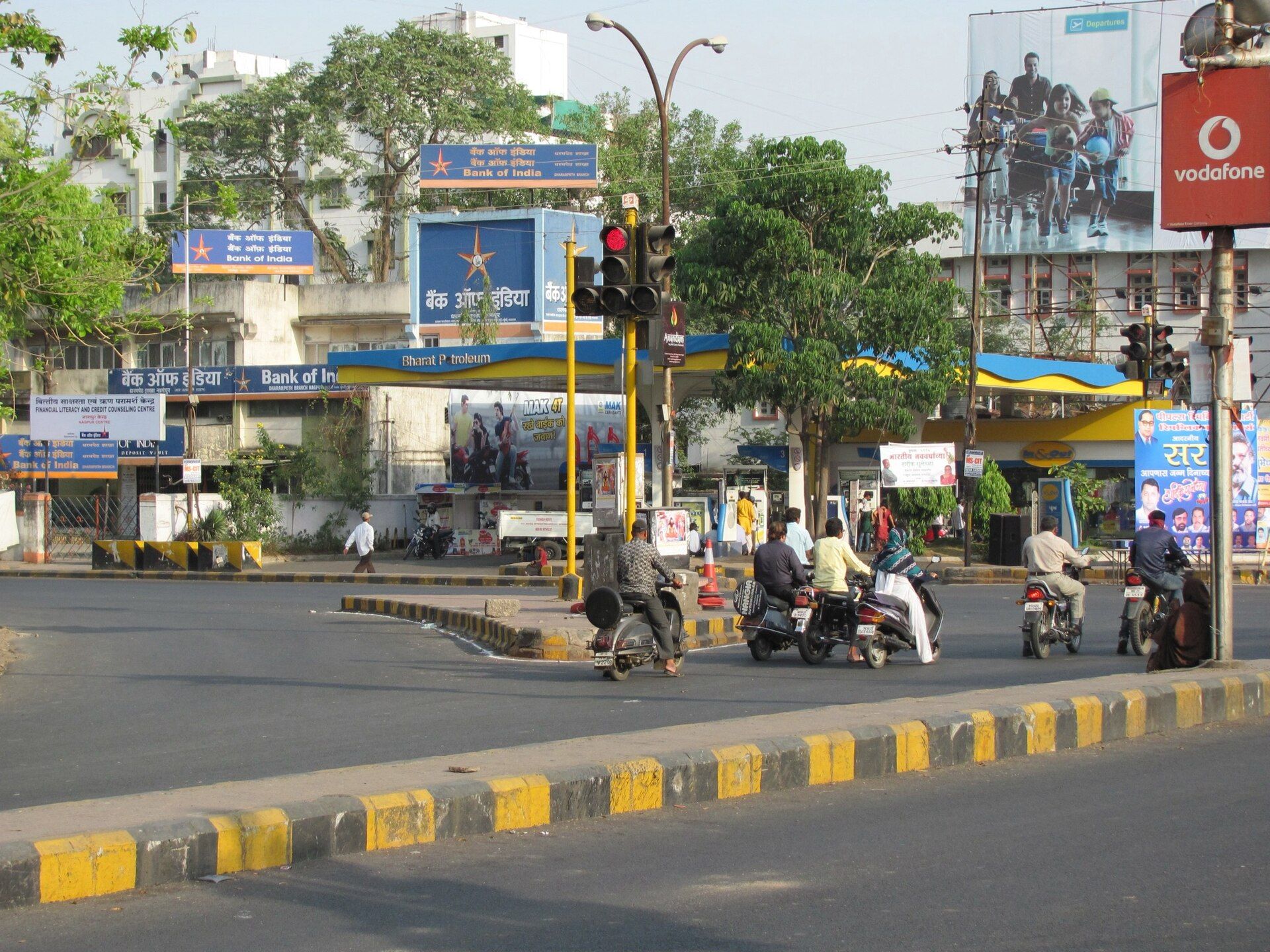 Street junction with a Bharat Petroleum petrol pump canopy, scooters waiting at a signal and Bank of India signs