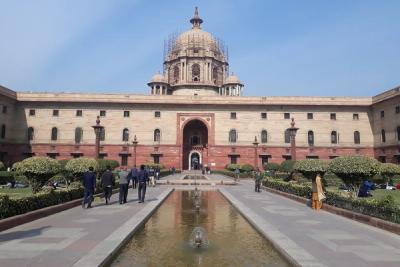 Sandstone North Block with a central dome and arched entrance, seen across a fountain pool with people on the paved paths