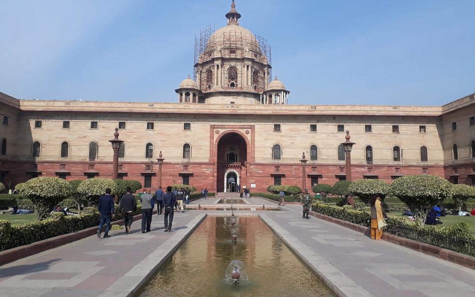 Sandstone North Block with a central dome and arched entrance, seen across a fountain pool with people on the paved paths