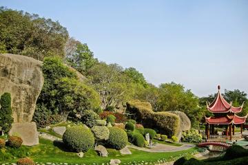 Landscaped garden with large boulders, clipped shrubs and a red pagoda beside a stone path under a clear sky