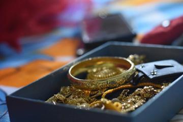 Gold bangle and gold chains heaped in a dark blue box, with blurred red and orange fabric behind
