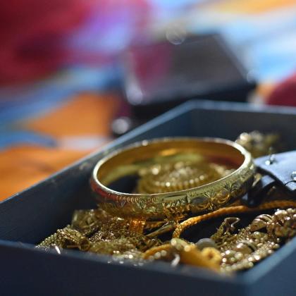 Gold bangle and gold chains heaped in a dark blue box, with blurred red and orange fabric behind