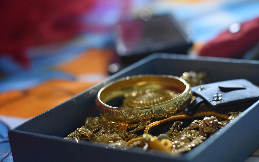 Gold bangle and gold chains heaped in a dark blue box, with blurred red and orange fabric behind