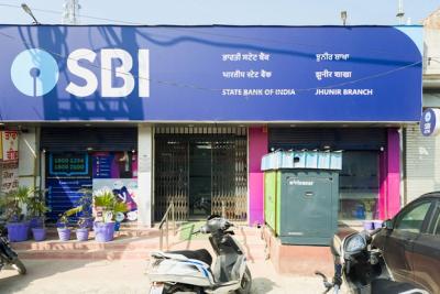Front of a State Bank of India branch with a blue SBI signboard, a kiosk, parked scooters and potted plants