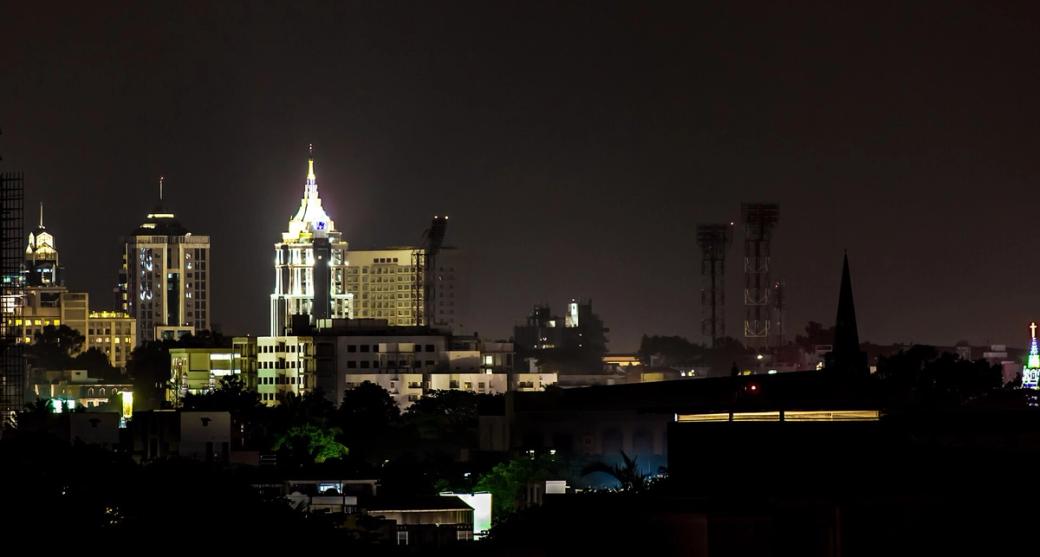 Night skyline of Bangalore with lit high-rise towers and a spire above dark rooftops and trees.
