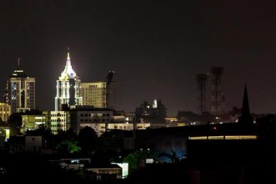 Night skyline of Bangalore with lit high-rise towers and a spire above dark rooftops and trees.