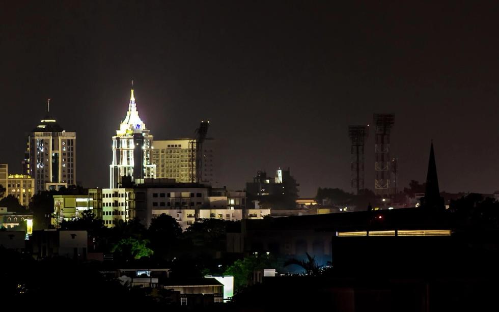 Night skyline of Bangalore with lit high-rise towers and a spire above dark rooftops and trees.