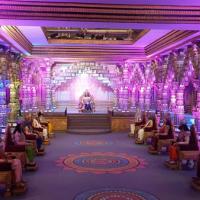 Ornate pillared hall lit in purple, with seated figures in traditional dress on a raised platform