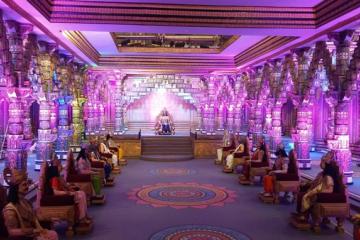Ornate pillared hall lit in purple, with seated figures in traditional dress on a raised platform