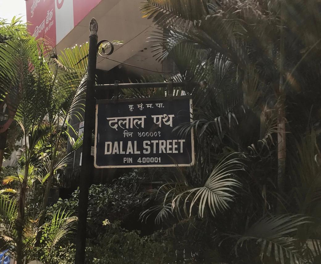 Blue Dalal Street sign in Hindi and English, with palm trees behind it.